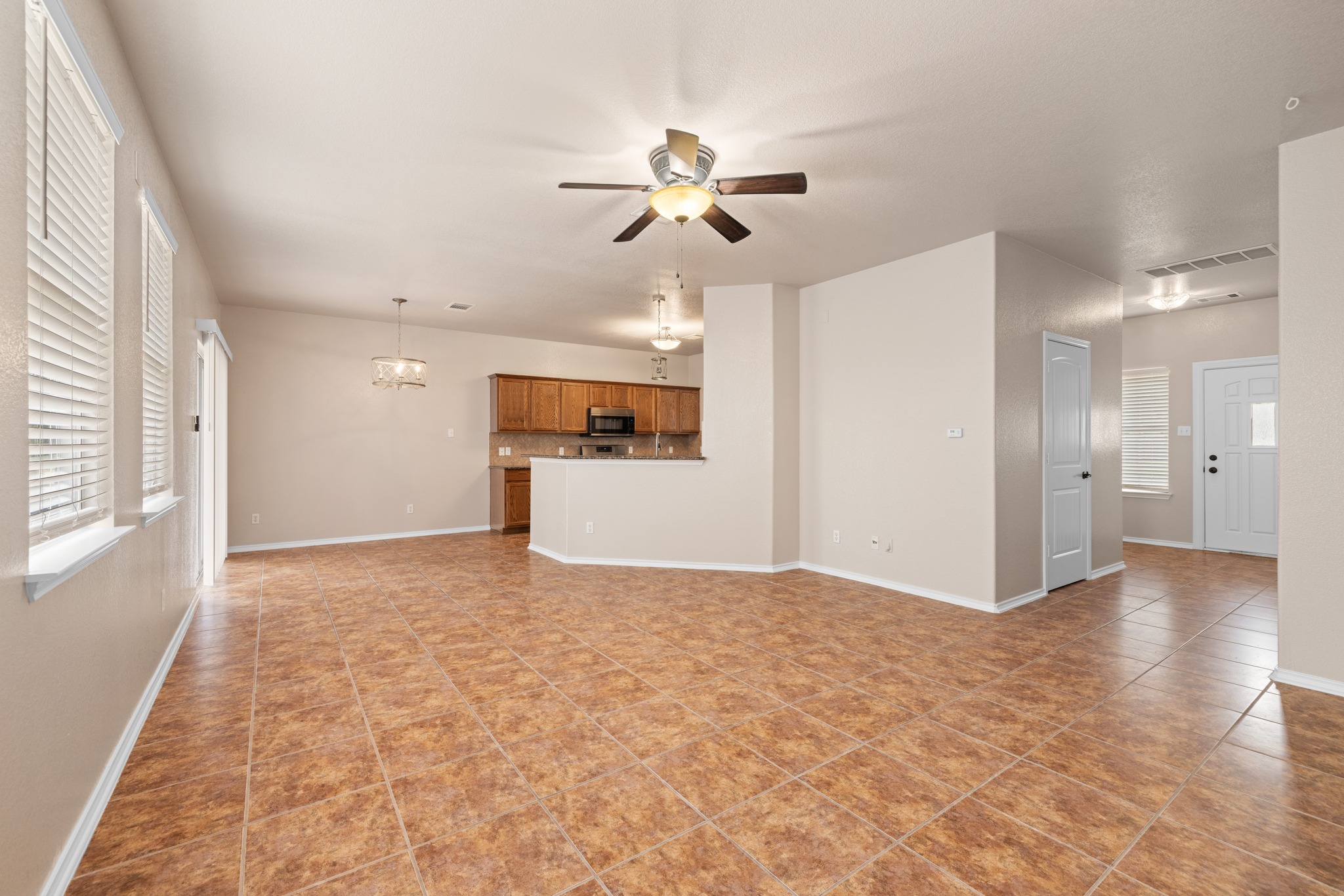 403 Red Hawk Drive Leander, TX 78641 - Photo 9 of 37 Spacious living area featuring tile flooring, neutral wall tones, multiple windows with blinds, a ceiling fan, and an open concept layout toward the kitchen