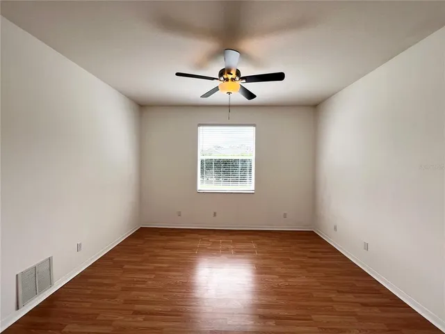 an empty room with wooden floor ceiling fan and window