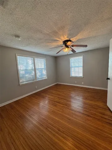 an empty room with wooden floor fan and windows
