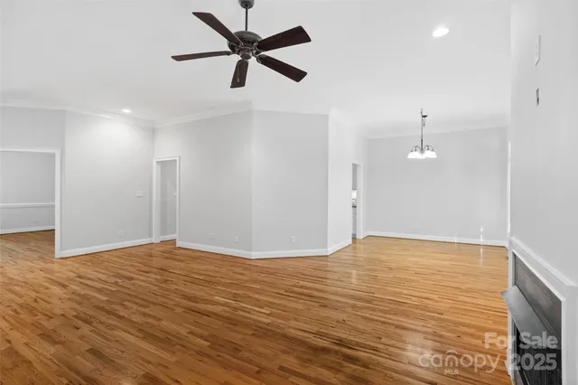 a view of an empty room with wooden floor and a ceiling fan