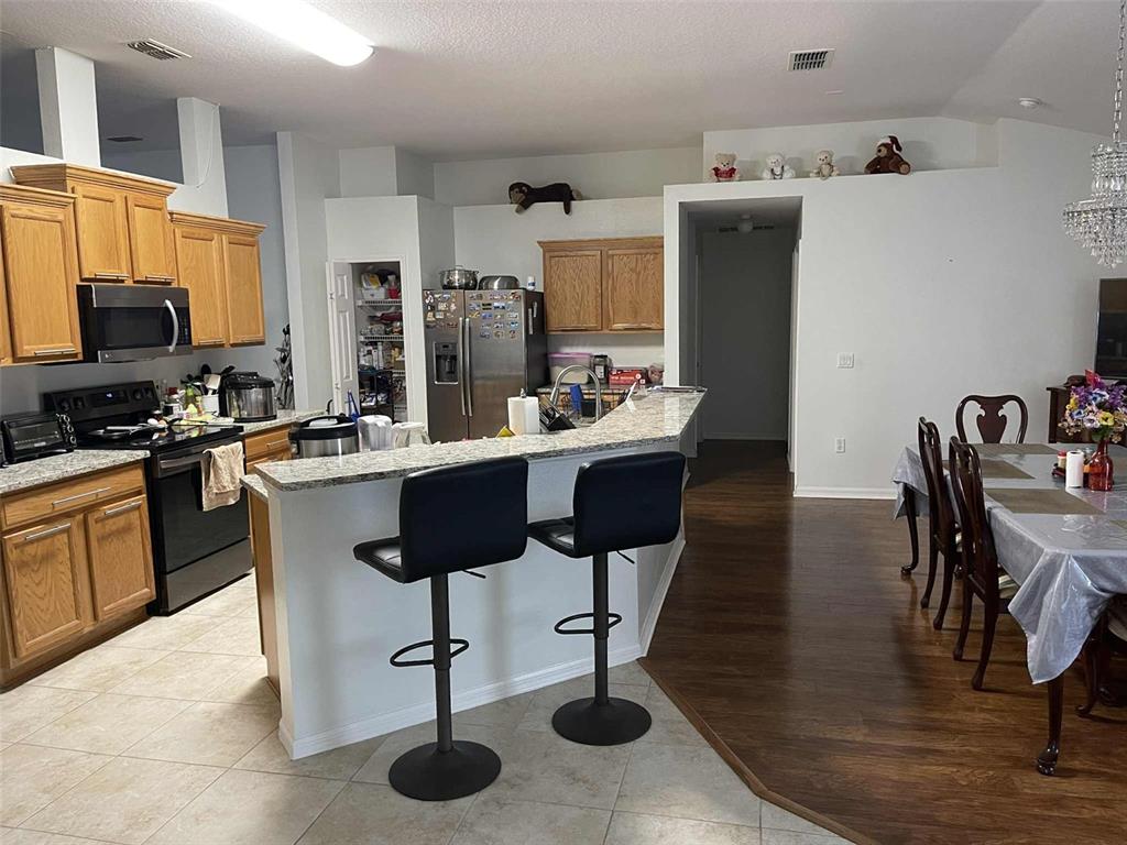 Undisclosed Address Palm Coast, FL 32164 - Photo 6 of 18 a kitchen with stainless steel appliances kitchen island granite countertop a sink dishwasher a stove a refrigerator a dining table and chairs with wooden floor