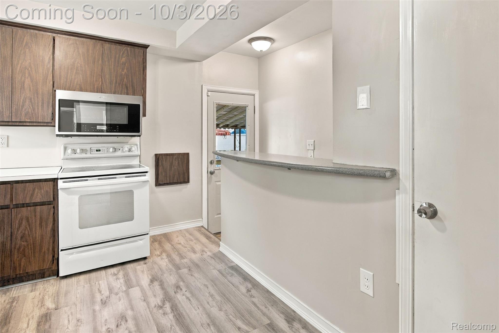 556 Henry Ruff Road Garden City, MI 48135 - Photo 6 of 49 Wood-finish cabinetry, stainless steel microwave, white electric range, light gray wood-finish flooring, and a breakfast bar