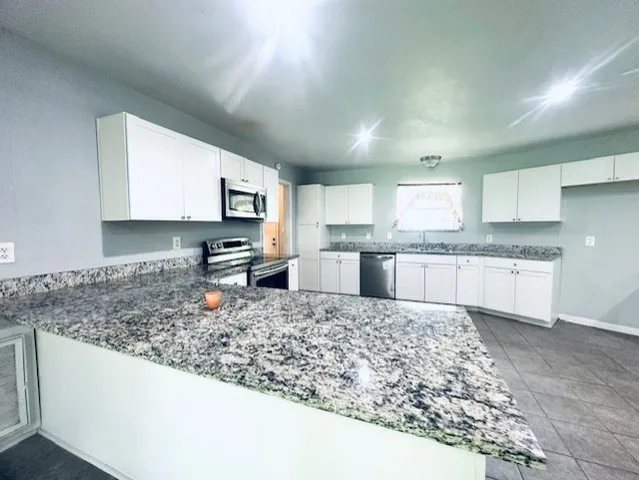 a large kitchen with granite countertop a counter top space cabinets and stainless steel appliances