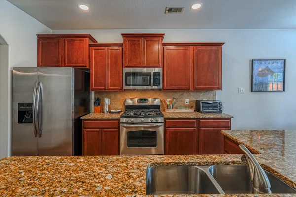 a kitchen with stainless steel appliances granite countertop a stove a refrigerator and a sink with wooden cabinets