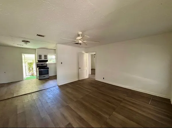 an empty room with wooden floor kitchen view and a window