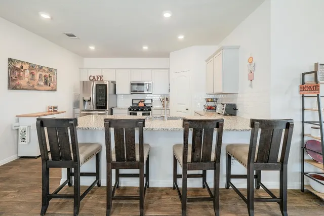 a kitchen with stainless steel appliances kitchen island granite countertop a dining table chairs and a refrigerator