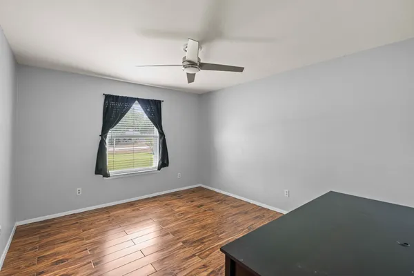 an empty room with wooden floor ceiling fan and windows