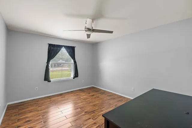 an empty room with wooden floor ceiling fan and windows