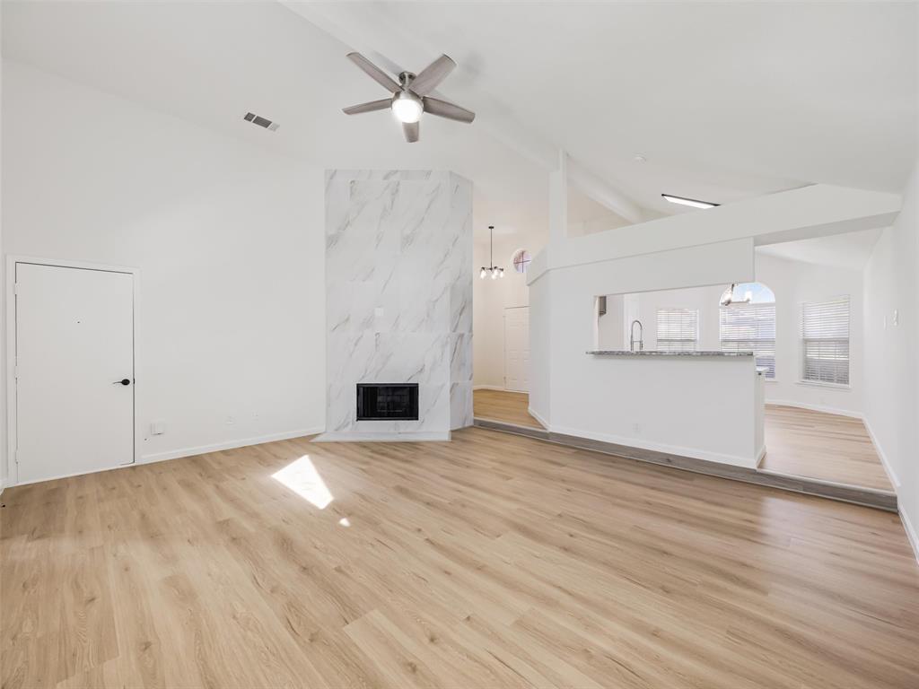 Vaulted ceilings with a ceiling fan, fireplace with a marble-finish surround, wood-finish flooring, and a breakfast bar with a stone-finish countertop