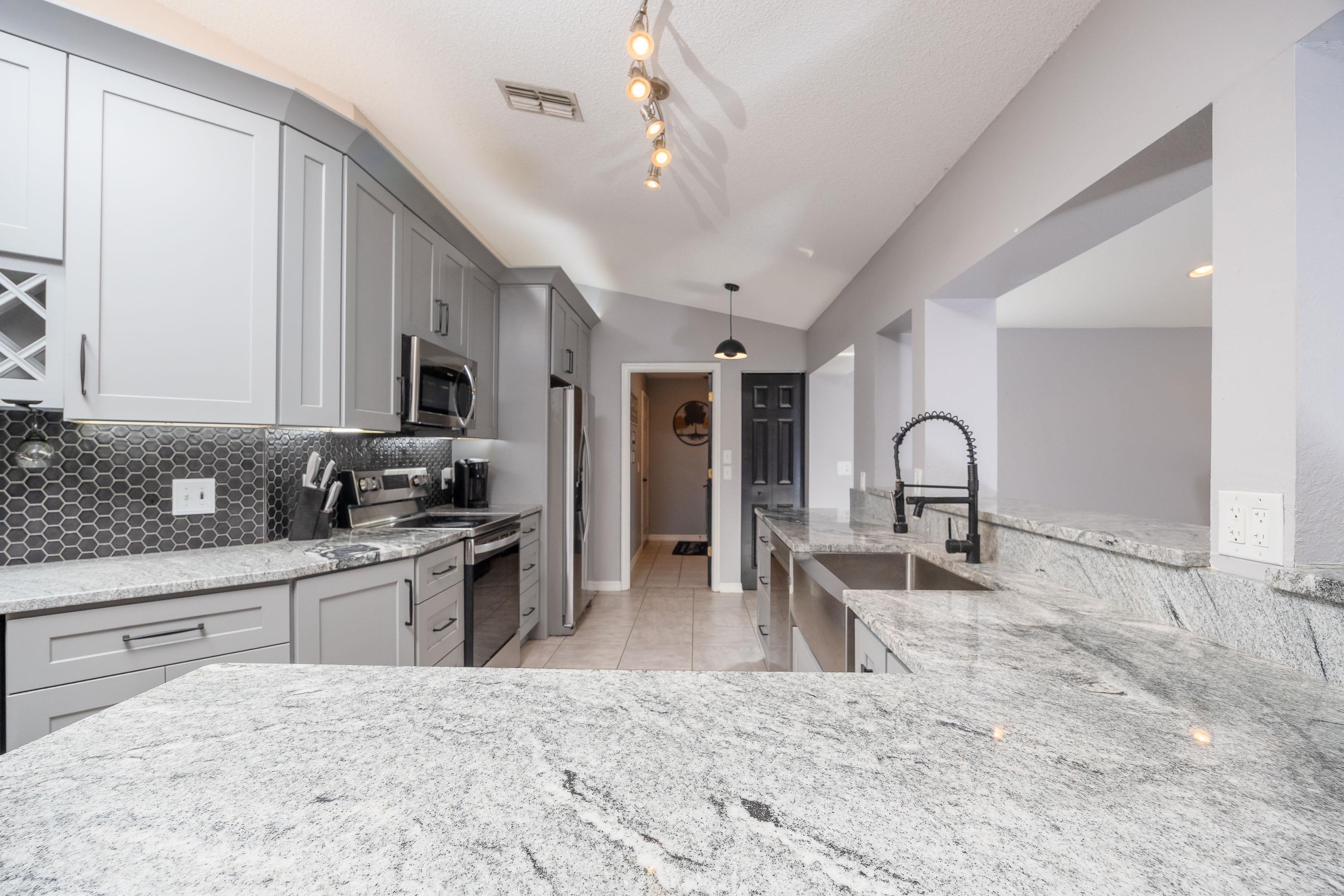 5 Rippling Place Palm Coast, FL 32164 - Photo 12 of 50 Kitchen featuring gray cabinets, appliances with stainless steel finishes, light stone countertops, lofted ceiling, and decorative light fixtures