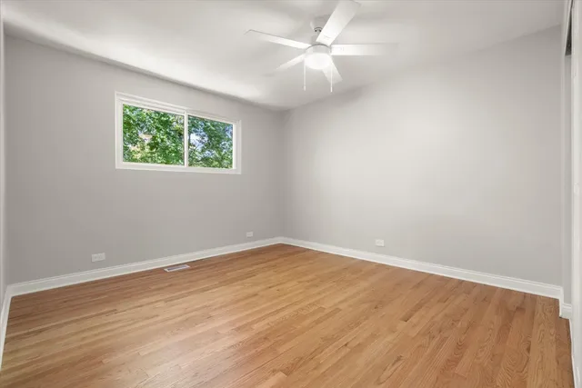 an empty room with wooden floor ceiling fan and windows