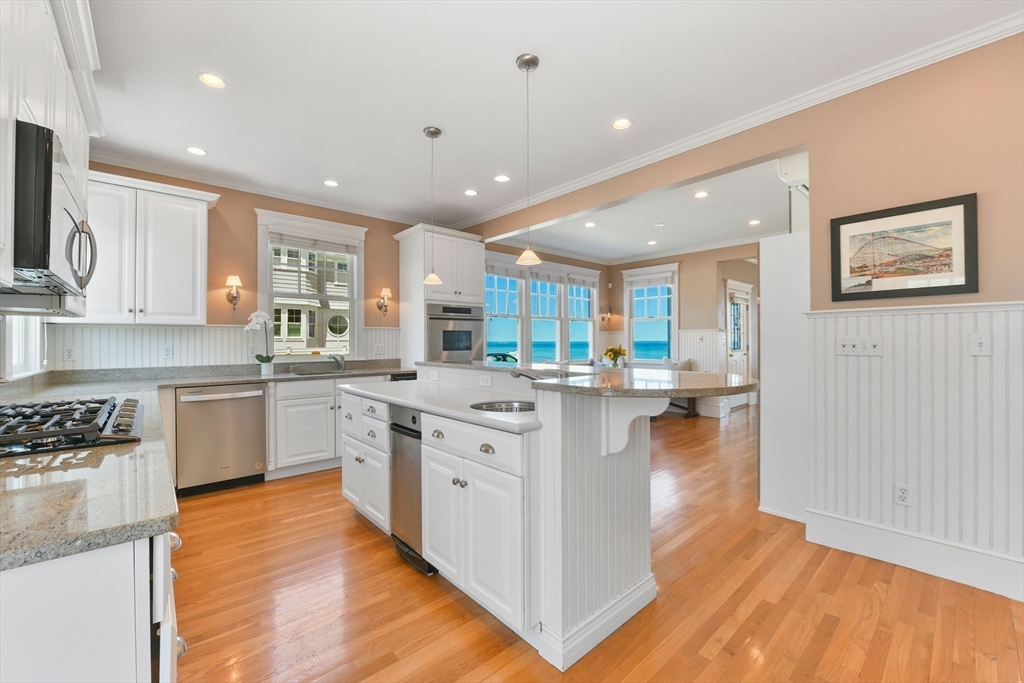 351 Beach Avenue Hull, MA 02045 - Photo 4 of 24 a kitchen with stainless steel appliances granite countertop a stove top oven a sink a refrigerator white cabinets and wooden floor next to a window