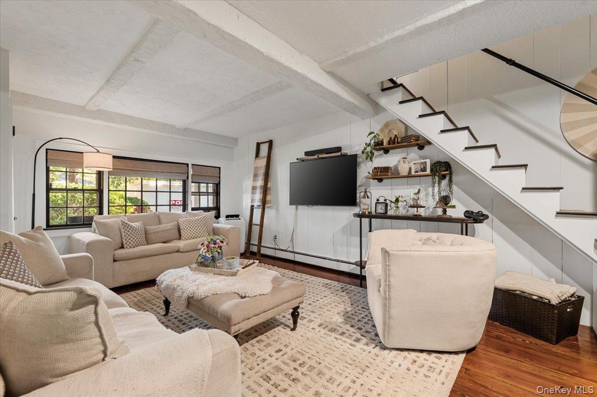 10 Rancher Place Huntington, NY 11743 - Photo 17 of 44 Open-concept living area featuring exposed ceiling beams, wood-finish flooring, and a staircase with painted risers