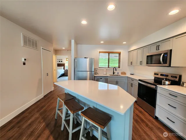 a kitchen with stainless steel appliances a stove a sink dishwasher a refrigerator white cabinets and wooden floor