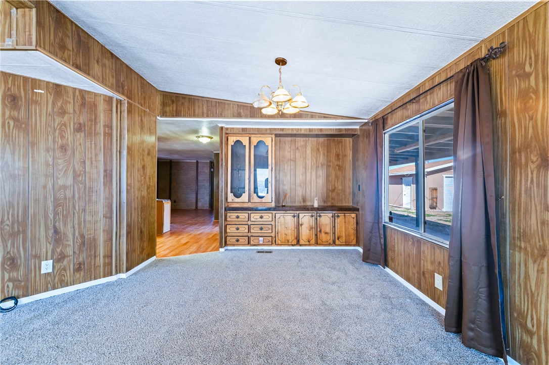 3475 Adobe Road Golden Valley, AZ 86413 - Photo 11 of 71 Empty room featuring wooden walls, vaulted ceiling, a chandelier, and light carpet