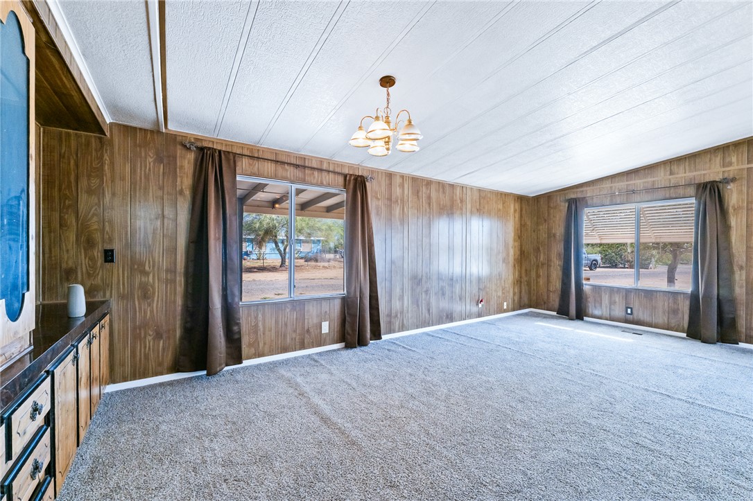 3475 Adobe Road Golden Valley, AZ 86413 - Photo 12 of 71 Spare room featuring a chandelier, wood walls, carpet, and a textured ceiling