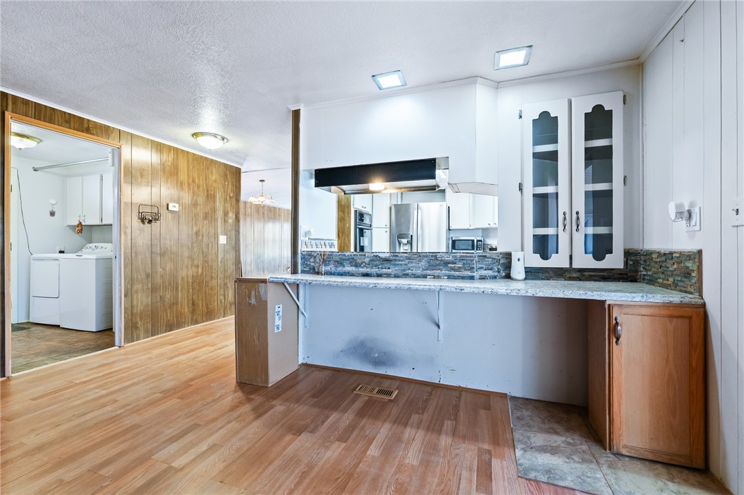 3475 Adobe Road Golden Valley, AZ 86413 - Photo 17 of 71 Kitchen with wooden walls, light wood-style floors, stainless steel appliances, a textured ceiling, and white cabinetry