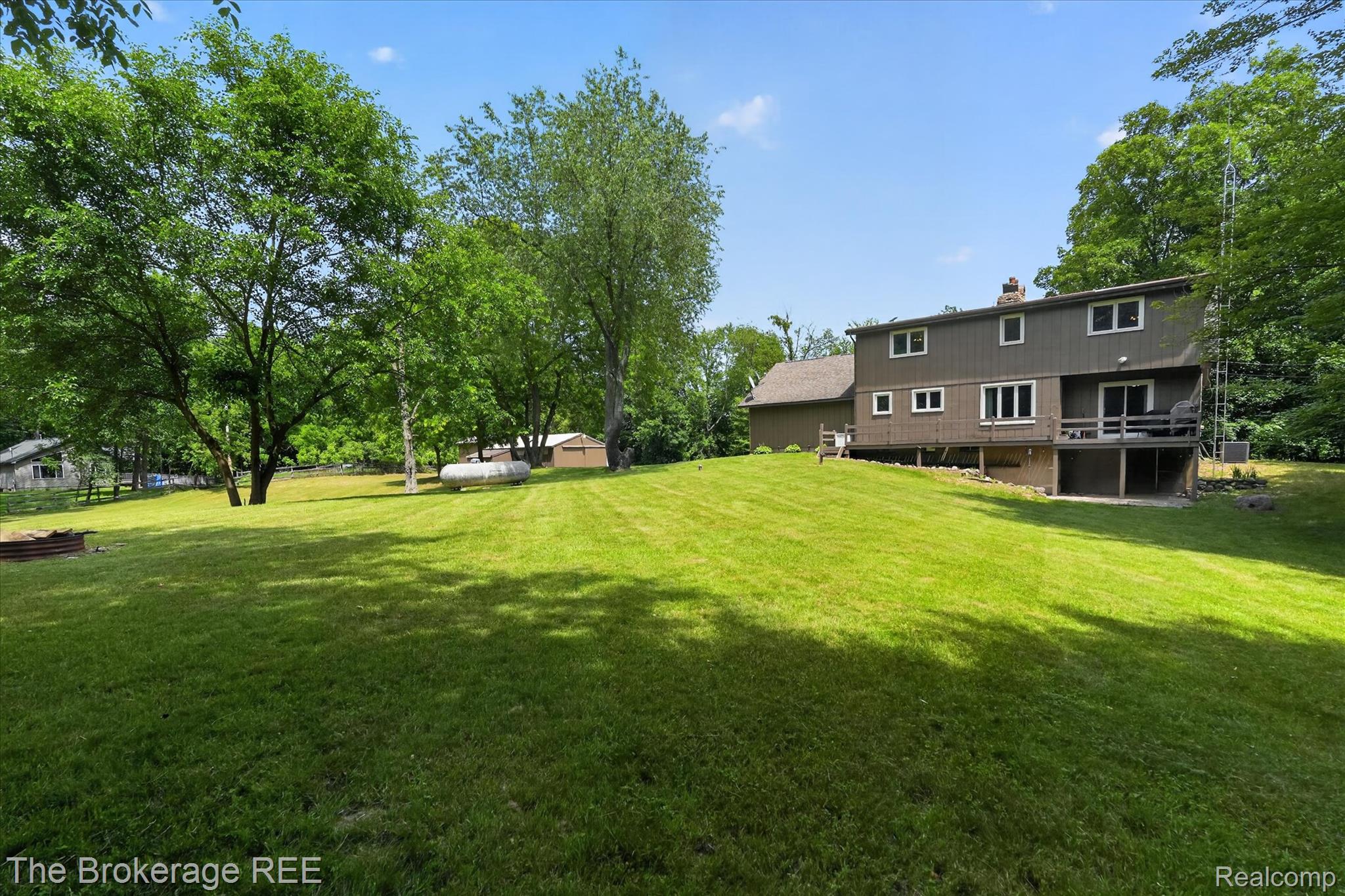 13269 North Genesee Road Clio, MI 48420 - Photo 49 of 67 Expansive rear yard featuring a sloped lawn, mature trees, and a two-story residence with a lower-level deck