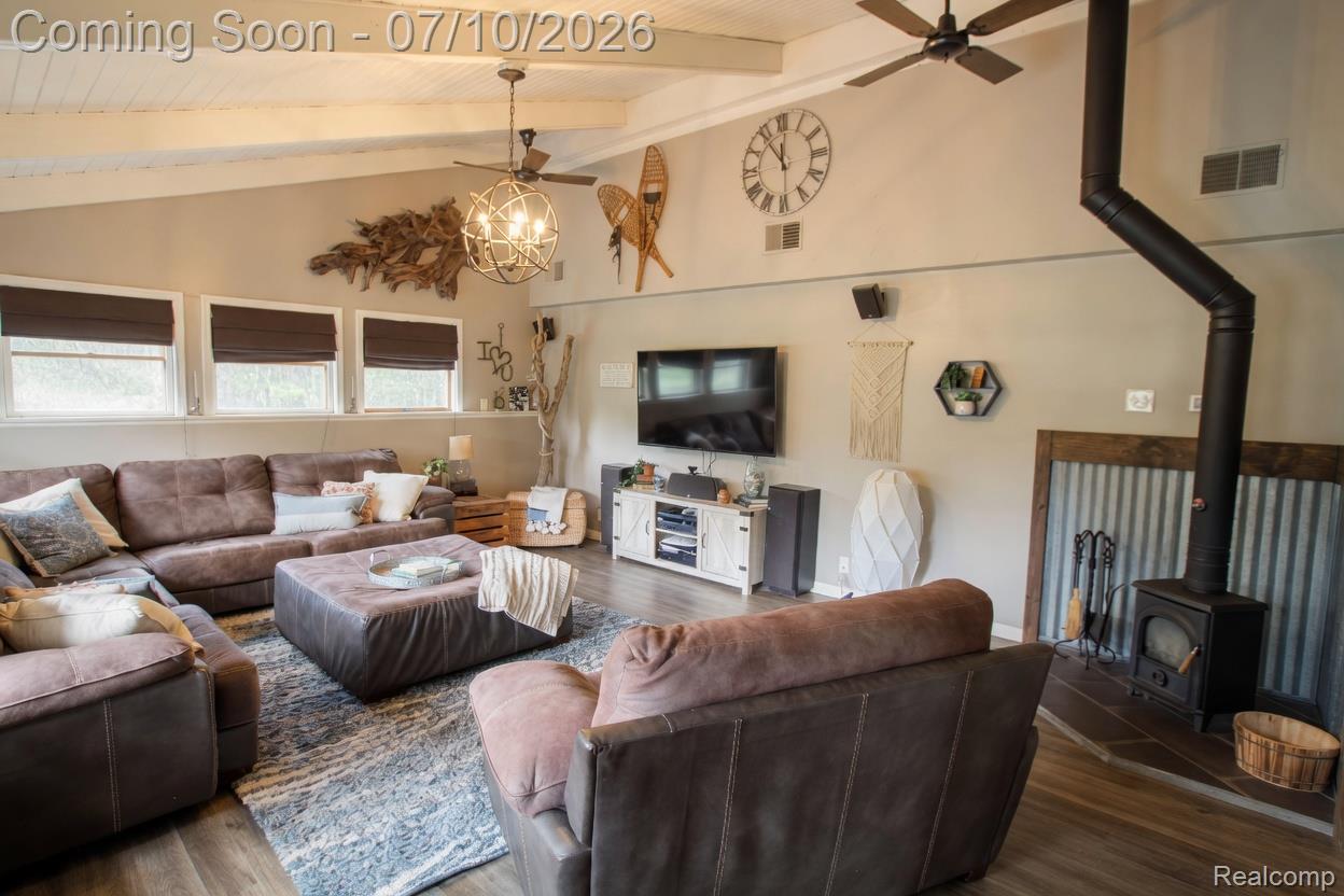 5278 Skelton Road Columbiaville, MI 48421 - Photo 29 of 64 Living area with wood-finish flooring, vaulted ceiling with exposed beams, and a black wood-burning stove with corrugated metal surround