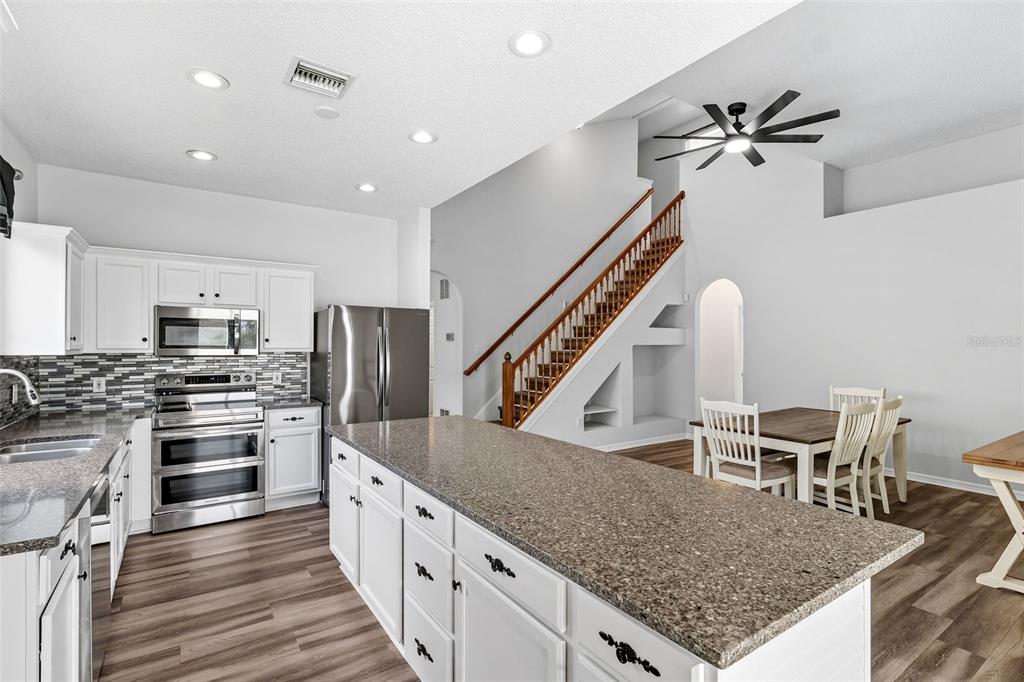 10443 Peppergrass Court Trinity, FL 34655 - Photo 17 of 62 a kitchen with stainless steel appliances kitchen island granite countertop a table chairs in it and wooden floors