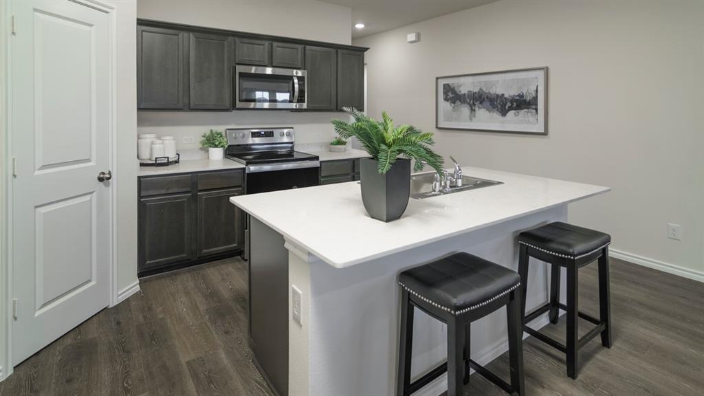 3100 Charleston Drive Ennis, TX 75119 - Photo 11 of 23 Kitchen featuring dark wood cabinetry, stainless steel appliances, a white solid surface island with an integrated sink, and wood-finish flooring