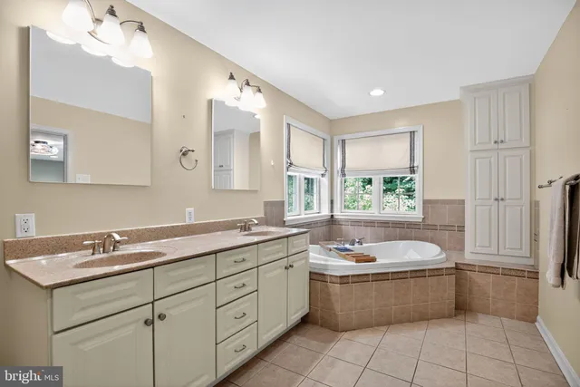 a bathroom with a granite countertop double vanity sink a mirror a bathtub and window