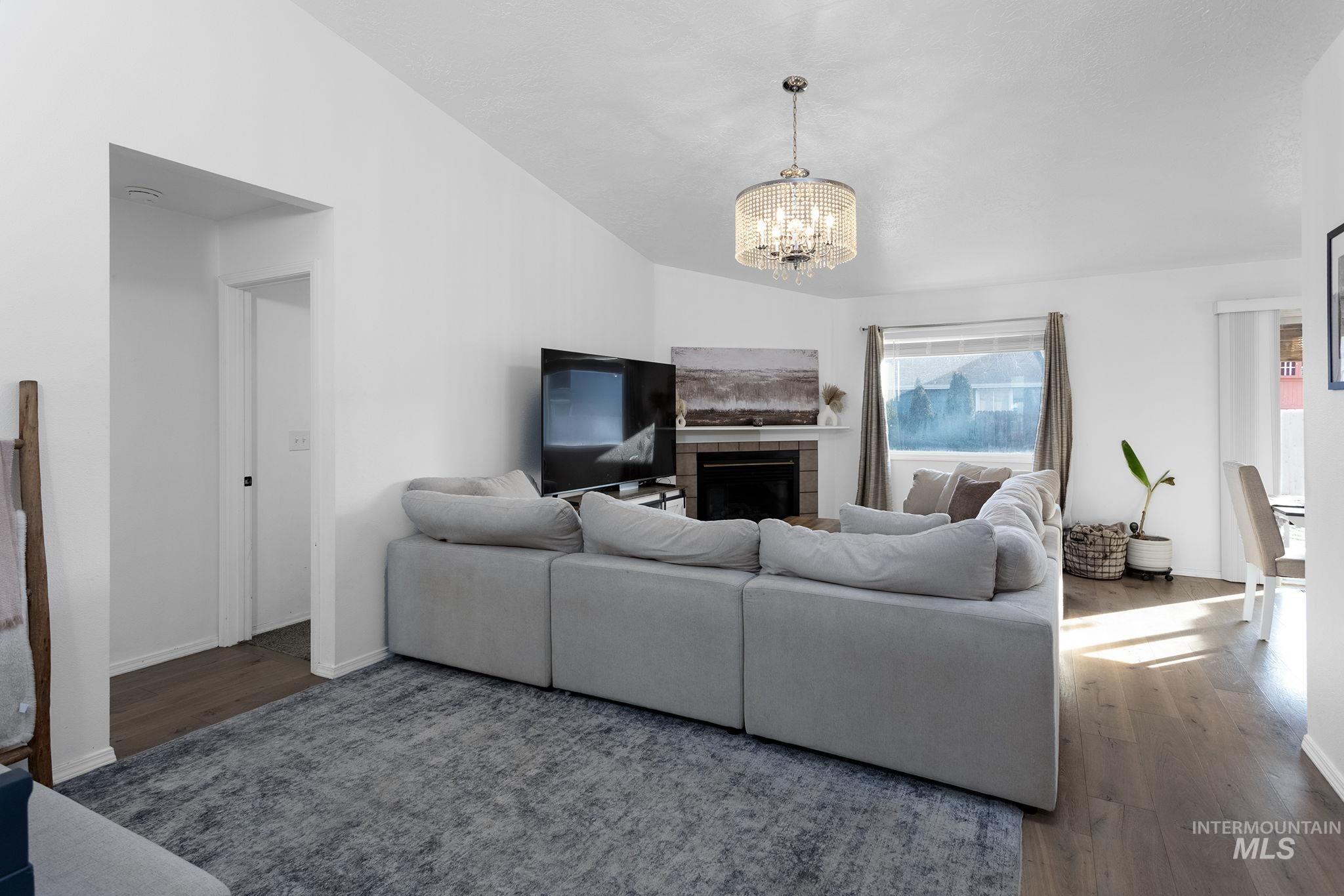 7899 West Prince Street Boise, ID 83714 - Photo 3 of 15 Living area featuring a tiled fireplace, a chandelier, and wood finished floors