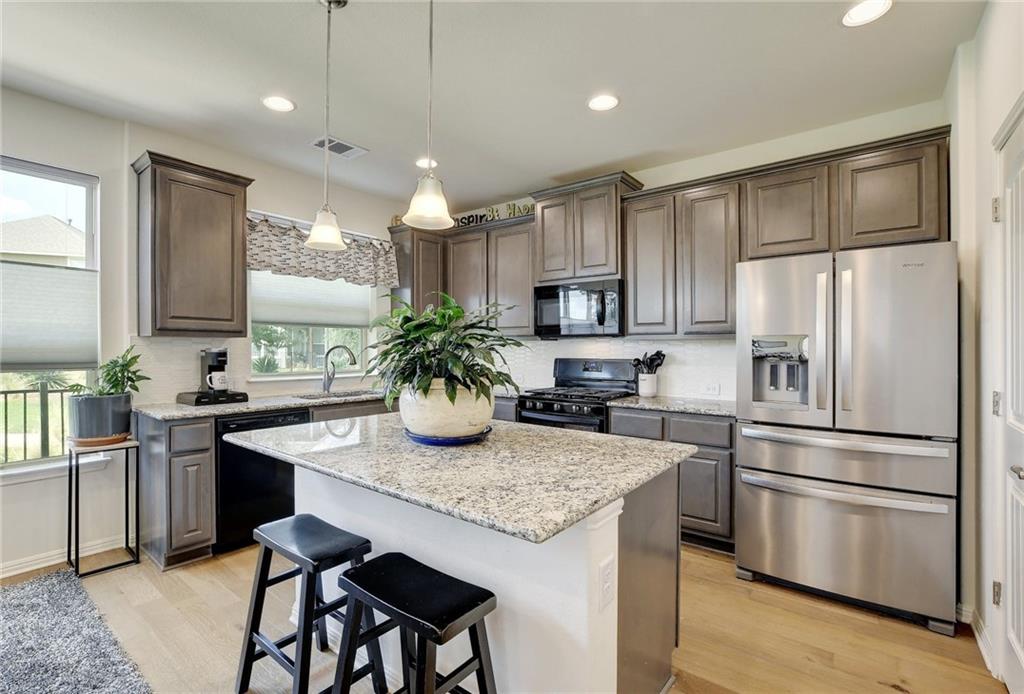 228 Simon Kyle, TX 78640 - Photo 5 of 35 Kitchen featuring black appliances, a breakfast bar, light wood-style flooring, hanging light fixtures, and a center island