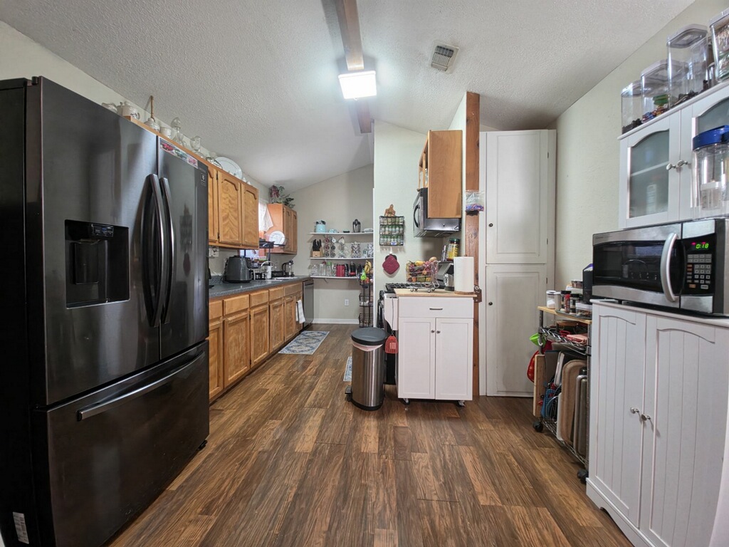 911 Brazos Street Lockhart, TX 78644 - Photo 19 of 22 The kitchen features a black stainless steel refrigerator, wood cabinetry, dark countertops, and wood-look flooring