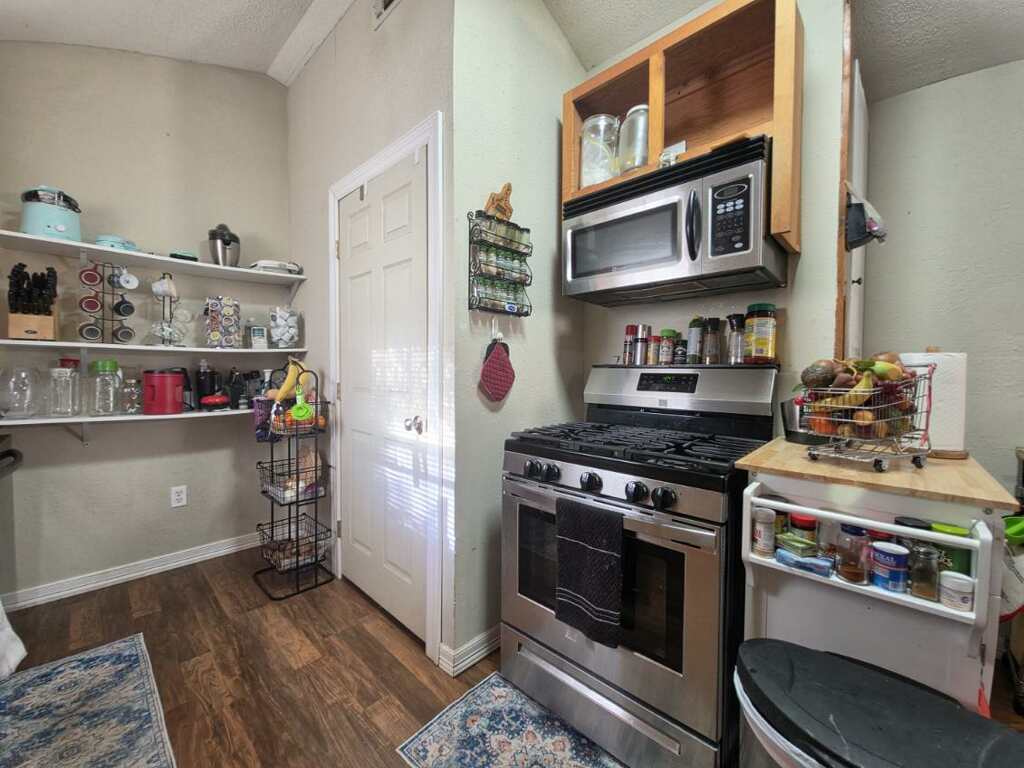 911 Brazos Street Lockhart, TX 78644 - Photo 21 of 22 The kitchen features stainless steel appliances including a range and an over-the-range microwave, wood-look flooring, and white shelving for storage