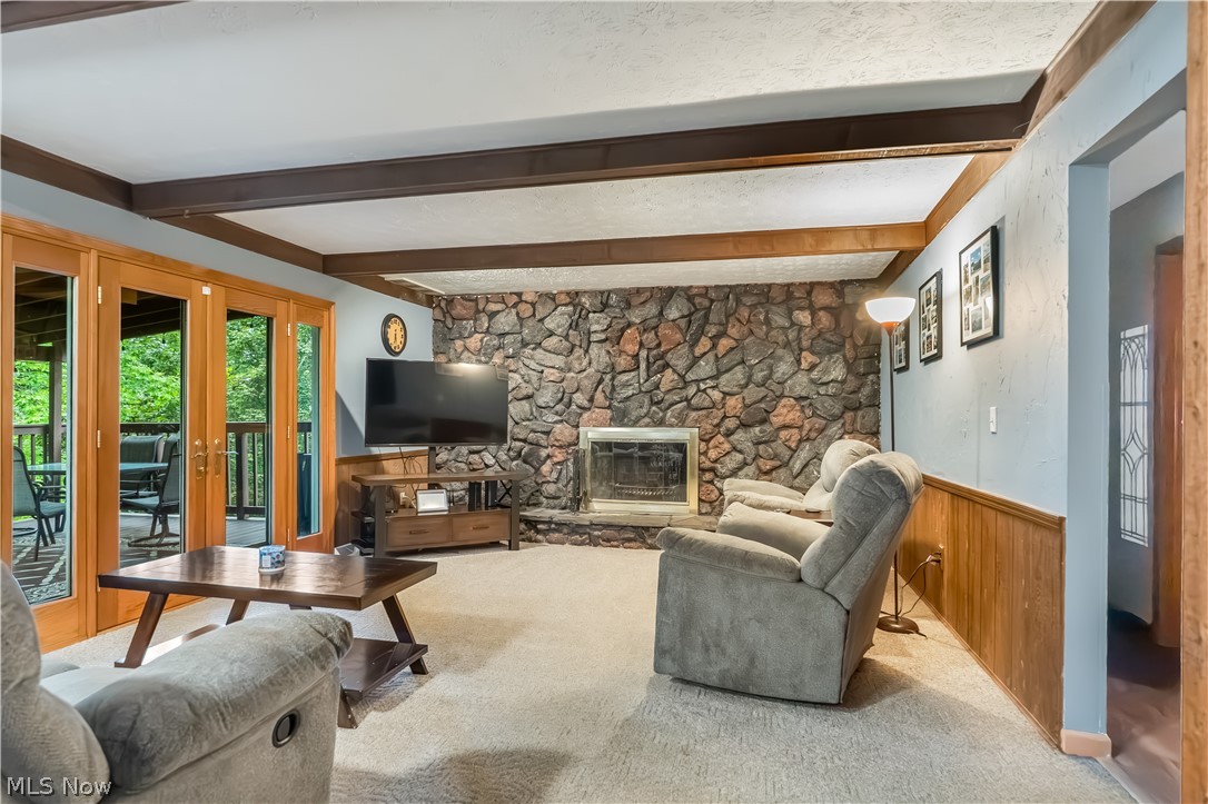 4922 South Ridge Road East Geneva, OH 44041 - Photo 11 of 46 Cozy family room featuring a floor-to-ceiling stone fireplace, rustic wood ceiling beams, and sliding glass doors that open to the back deck.