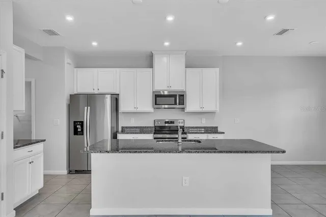 a kitchen with stainless steel appliances granite countertop a stove a sink a refrigerator and white cabinets