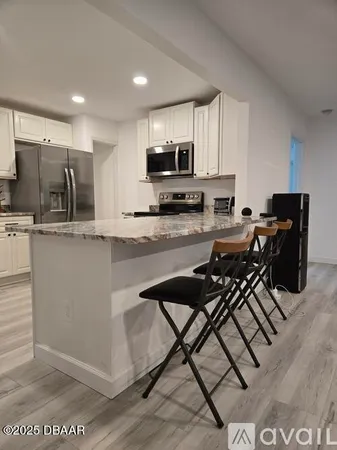 a kitchen with stainless steel appliances granite countertop a stove top oven a sink a refrigerator white cabinets and granite countertops with wooden floor