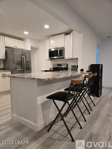 a kitchen with stainless steel appliances granite countertop a stove top oven a sink a refrigerator white cabinets and granite countertops with wooden floor