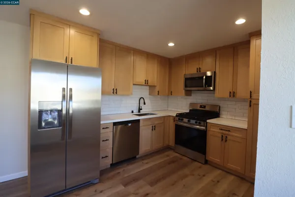 a kitchen with stainless steel appliances granite countertop a refrigerator a sink a stove a microwave and island with wooden floor