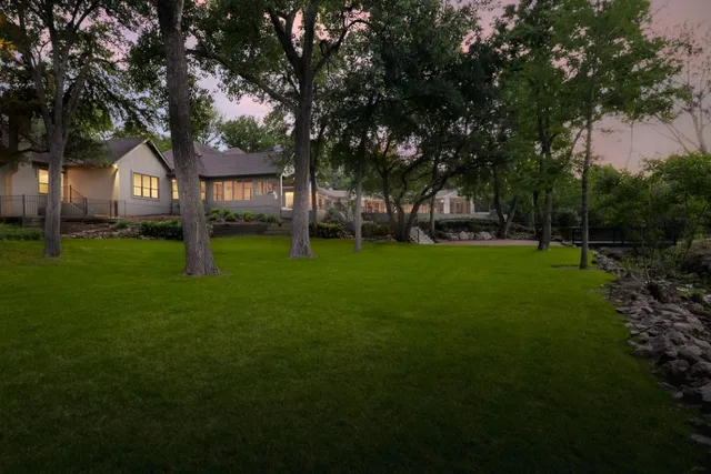 a view of a tree in front of a house with a big yard and large trees