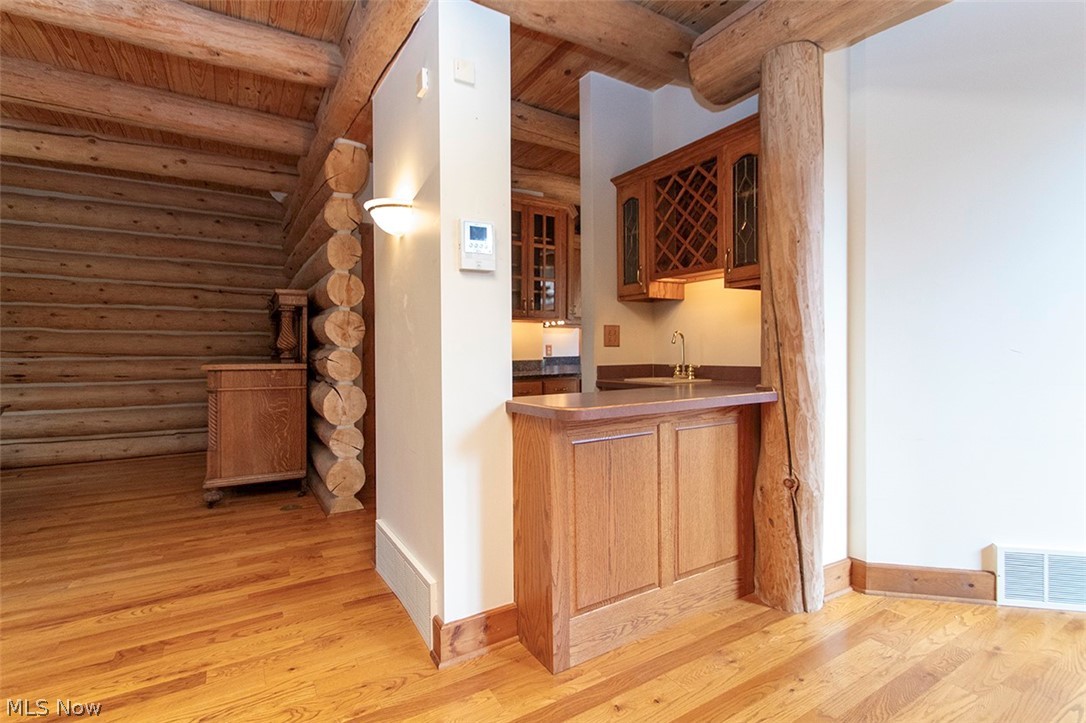 1871 Mattingly Road Hinckley, OH 44233 - Photo 14 of 50 Indoor wet bar with rustic walls, light wood-style floors, glass fronted cabinets, wood finish cabinetry, and beam ceiling
