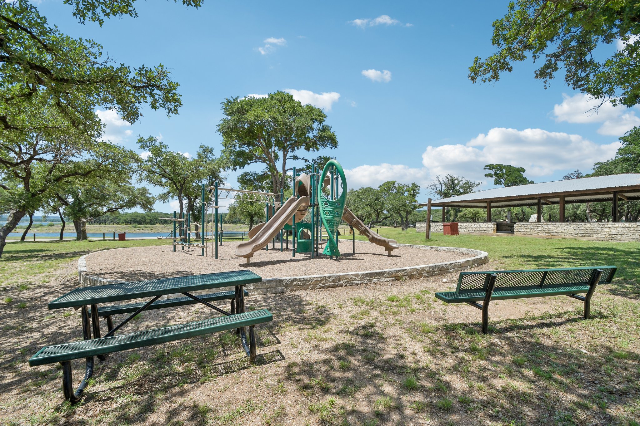 20609 Bridle Path Road Lago Vista, TX 78645 - Photo 28 of 30 A vibrant playground set amidst a natural landscape with mature trees and a tranquil body of water nearby.