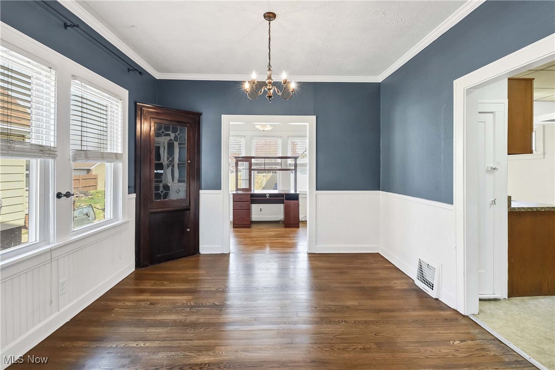 7700 Spring Garden Road Cleveland, OH 44129 - Photo 11 of 50 Unfurnished dining area featuring dark wood-style floors, a chandelier, a wainscoted wall, and ornamental molding
