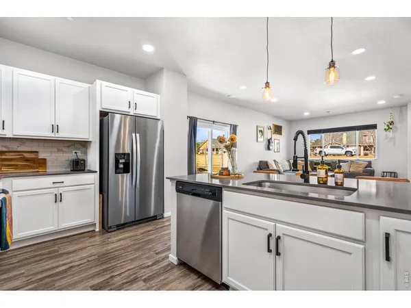 a kitchen with stainless steel appliances granite countertop a refrigerator a sink dishwasher a stove and white cabinets with wooden floor