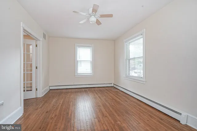 an empty room with wooden floor ceiling fan and windows