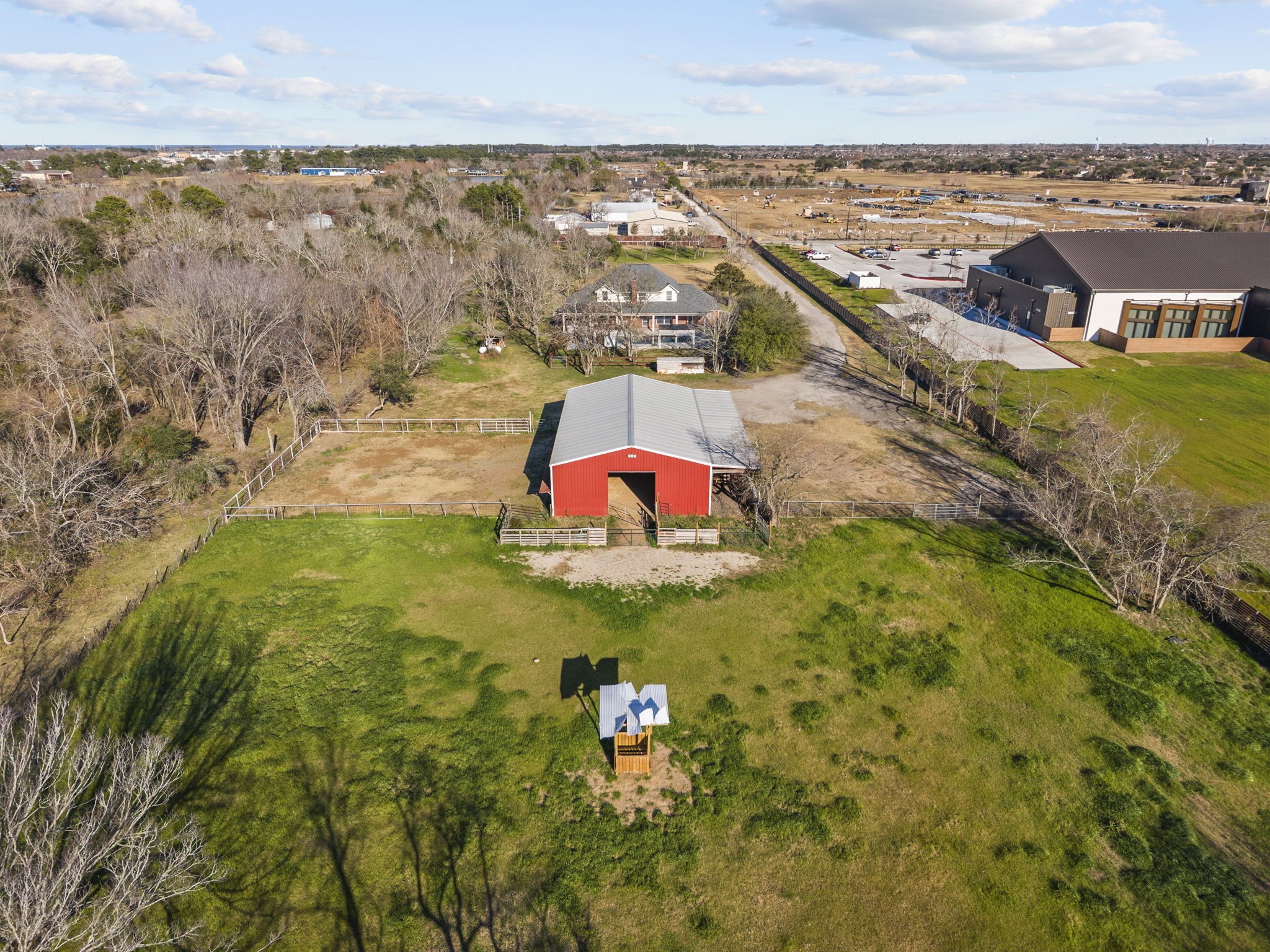2730 Lawrence Road Kemah, TX 77565 - Photo 7 of 46 This aerial view showcases a spacious property featuring a vibrant red barn, fenced areas, and wide-open green spaces, ideal for country living. The surrounding landscape includes trees and neighboring structures, offering both privacy and community access.
