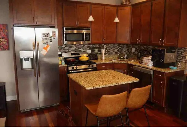 a kitchen with stainless steel appliances granite countertop a refrigerator a sink a stove a dining table and chairs