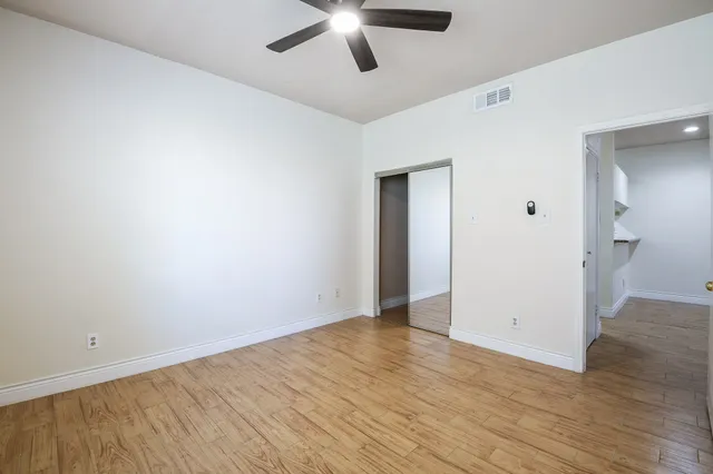 an empty room with wooden floor and a ceiling fan