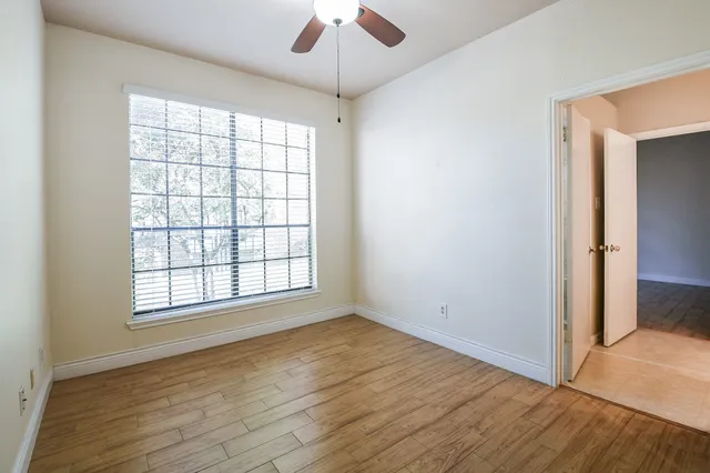 an empty room with wooden floor chandelier fan and windows