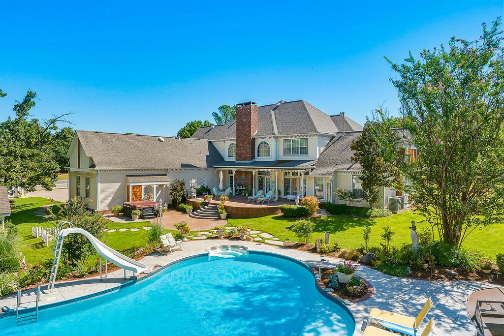 Expansive backyard featuring a custom-shaped swimming pool, integrated spa, tiered patio, and a manicured lawn