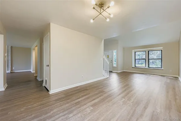 an empty room with wooden floor chandelier and windows