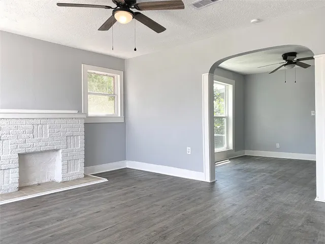 an empty room with wooden floor fan and windows