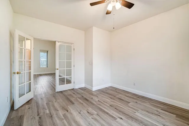 an empty room with wooden floor chandelier fan and windows