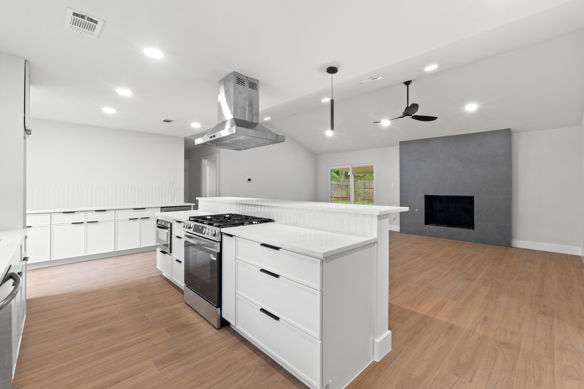 1608 Springer Lane Austin, TX 78758 - Photo 24 of 35 Open-concept kitchen featuring an island with built-in range, stainless steel appliances, white cabinetry, and wood-finish flooring